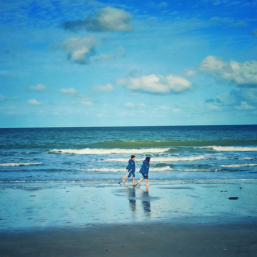 zwei Jungen gehen barfuß den Strand entlang